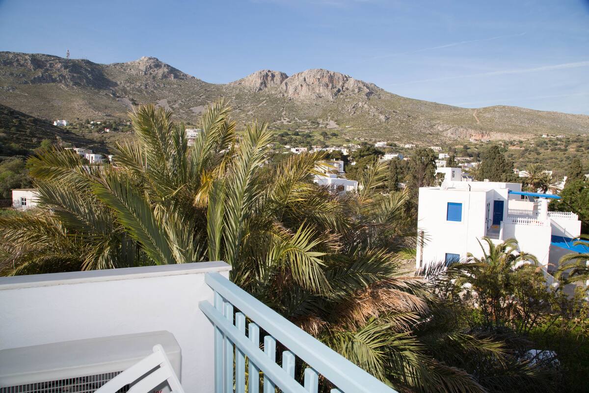 A coastal town with white buildings, palm trees, and mountains in the background.