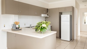A modern kitchen with a central island, built-in cabinets, a refrigerator, and a sink. - Townsville Southbank Apartments (South Townsville)