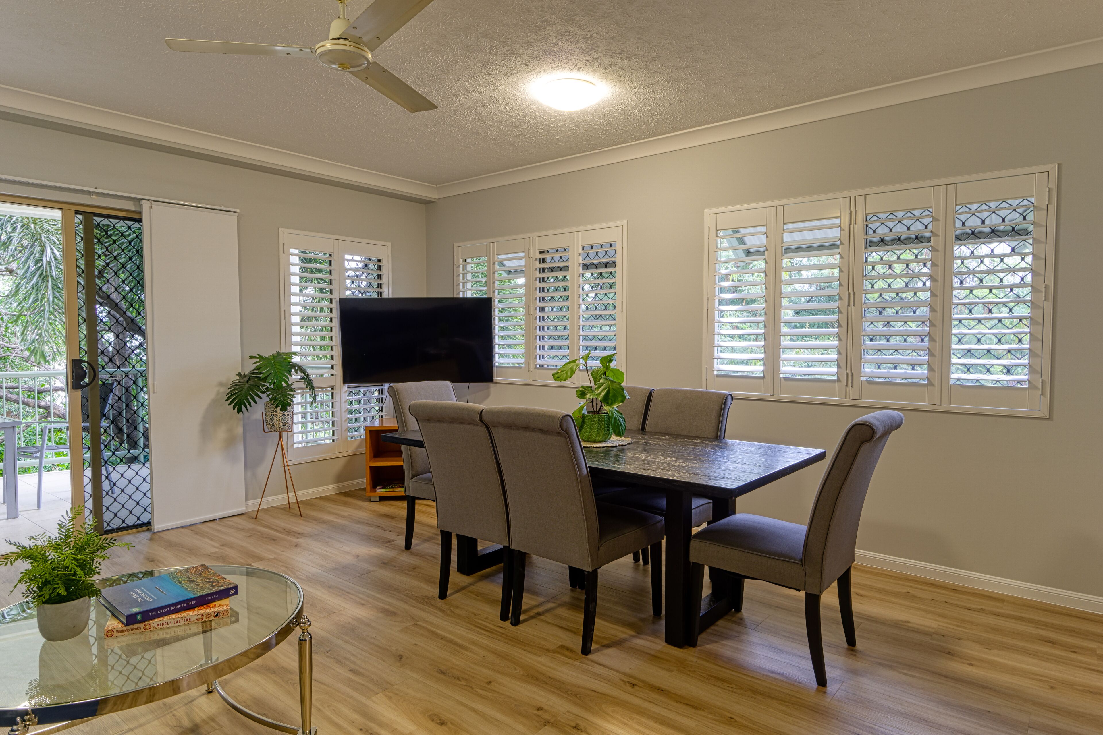 A dining area with a table and chairs, a ceiling fan, and a television.
