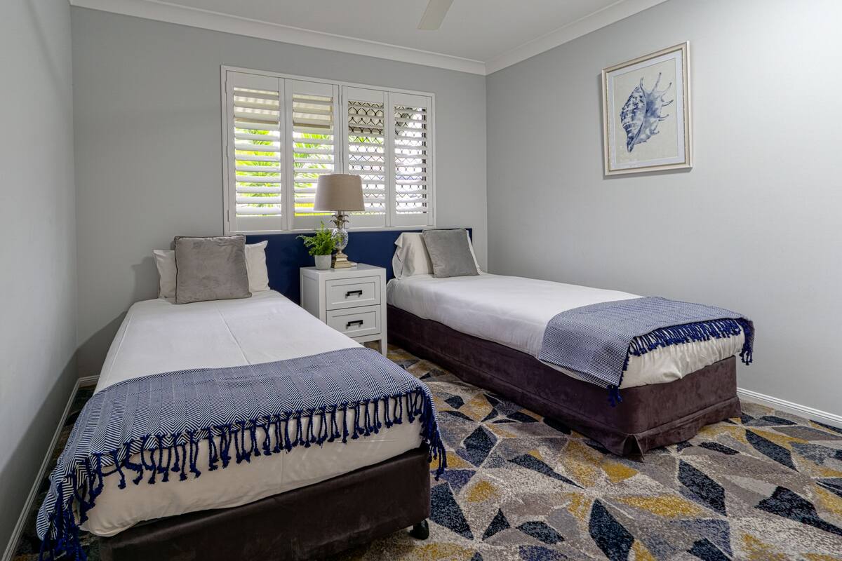 Une chambre avec deux lits, une table de chevet, une lampe et une fenêtre avec des volets.