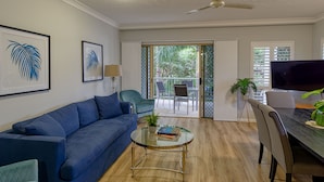 A living room with a blue sofa, a glass coffee table, and a ceiling fan. - Townsville Southbank Apartments (South Townsville)