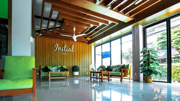 Um lobby moderno com teto de madeira, sofá verde, cadeiras de madeira e uma grande janela com vista para o verde.