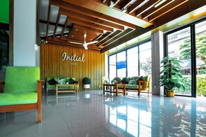 A modern lobby with a wooden ceiling, a green sofa, wooden chairs, and a large window with a view of greenery. - Initial Hua Hin (Hua Hin)