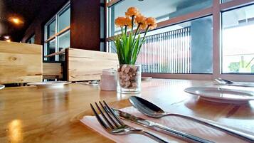 A dining table with cutlery, a glass vase with flowers, and a window with a view of the outside.