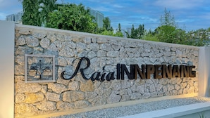 A stone wall with the words "Rac Inn Penang" in large letters, a framed picture, and a view of buildings and trees in the background. - Raia Inn Penang (George Town)