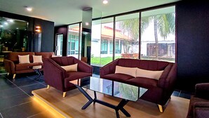 A modern lobby with dark-toned sofas, a glass coffee table, and large windows offering a view of a building and greenery outside. - Raia Inn Penang (George Town)