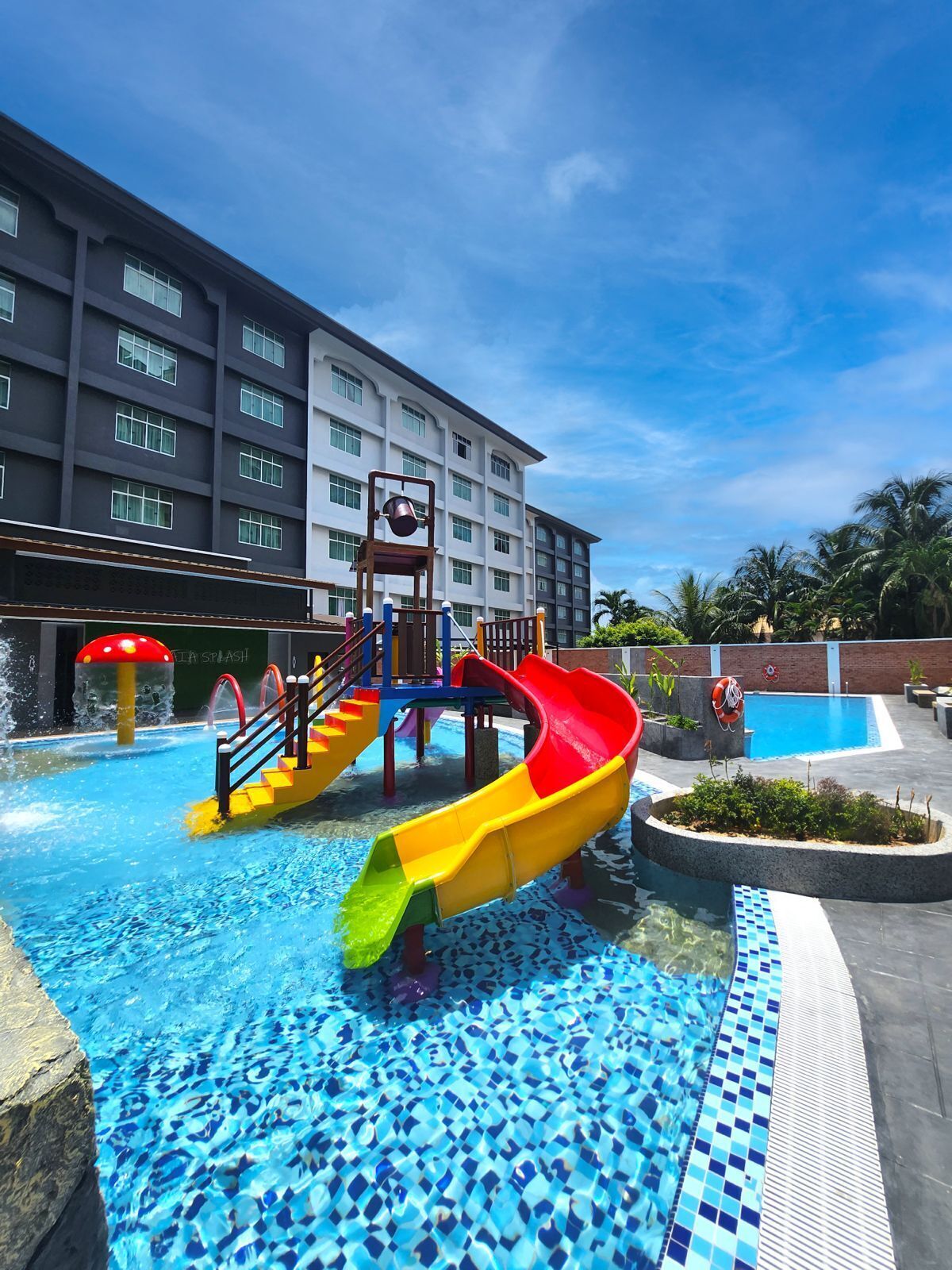 Zona de piscina de hotel con tobogán de agua, área de juegos para niños y piscina con mosaicos azules.