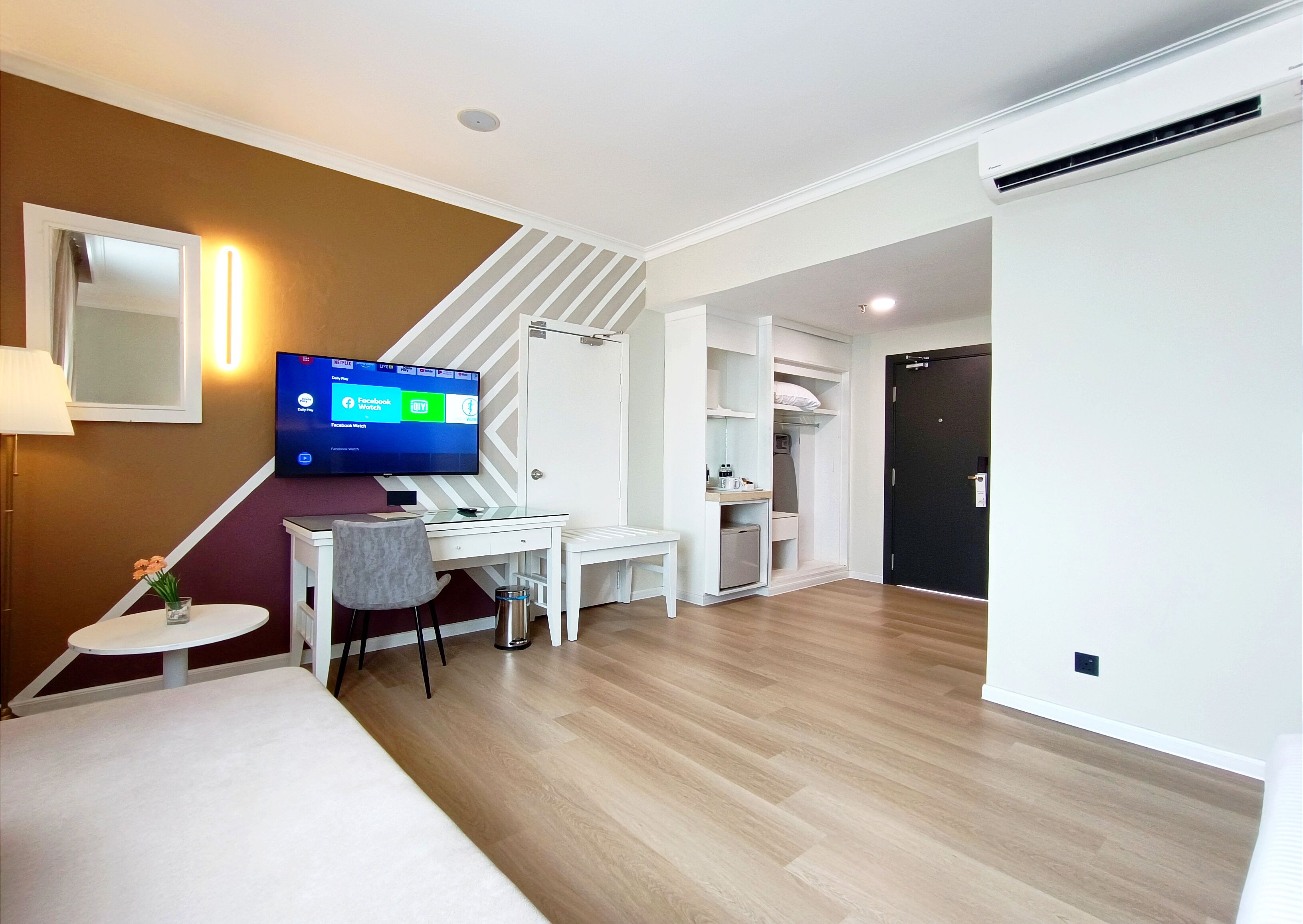 A modern living room with a flat-screen TV, a desk, and a staircase leading to a bedroom.