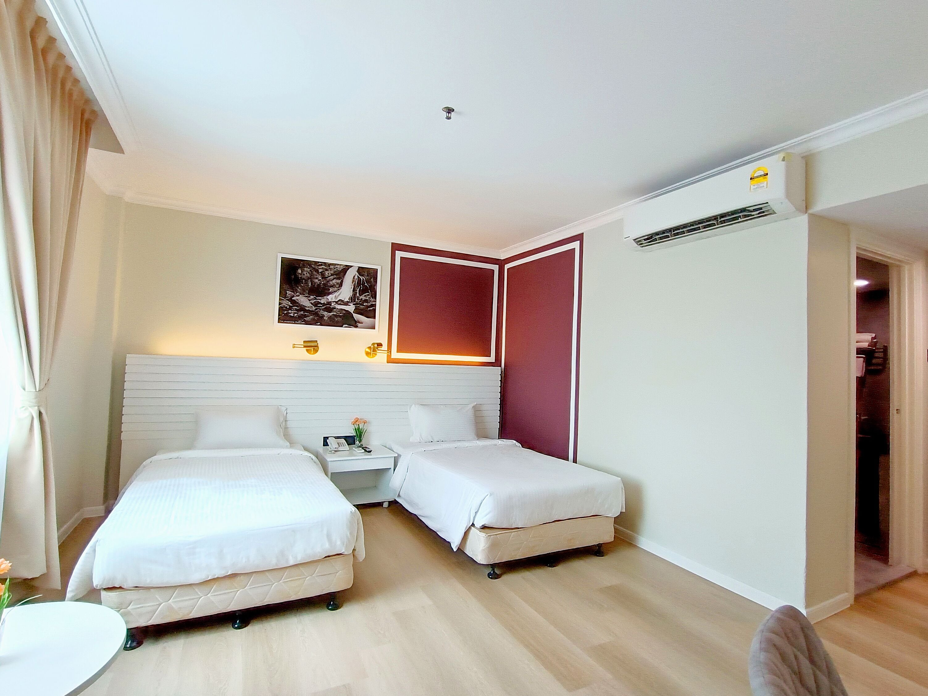 Habitación de hotel con dos camas, una mesita de noche con lámpara, un cuadro en la pared y un equipo de aire acondicionado.