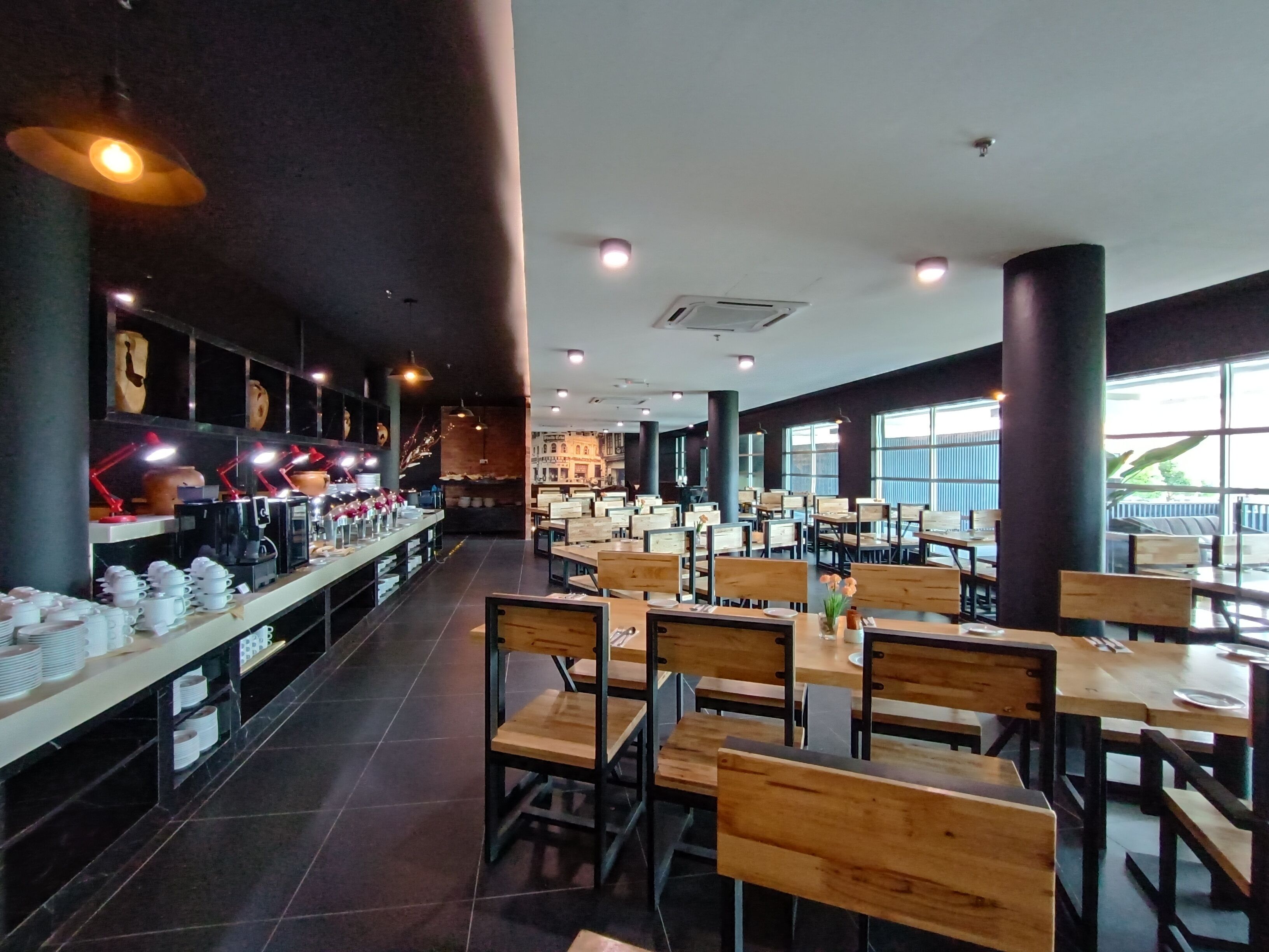 Un restaurant spacieux avec des tables et des chaises hautes, un long comptoir équipé de matériel de cuisine et de grandes fenêtres laissant entrer la lumière naturelle.