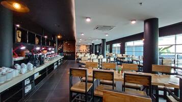 Un restaurante espacioso con mesas y sillas altas, una barra larga con equipo de cocina y ventanas grandes que dejan entrar luz natural.