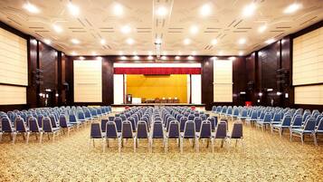 A large conference room with rows of chairs facing a stage with a red curtain.