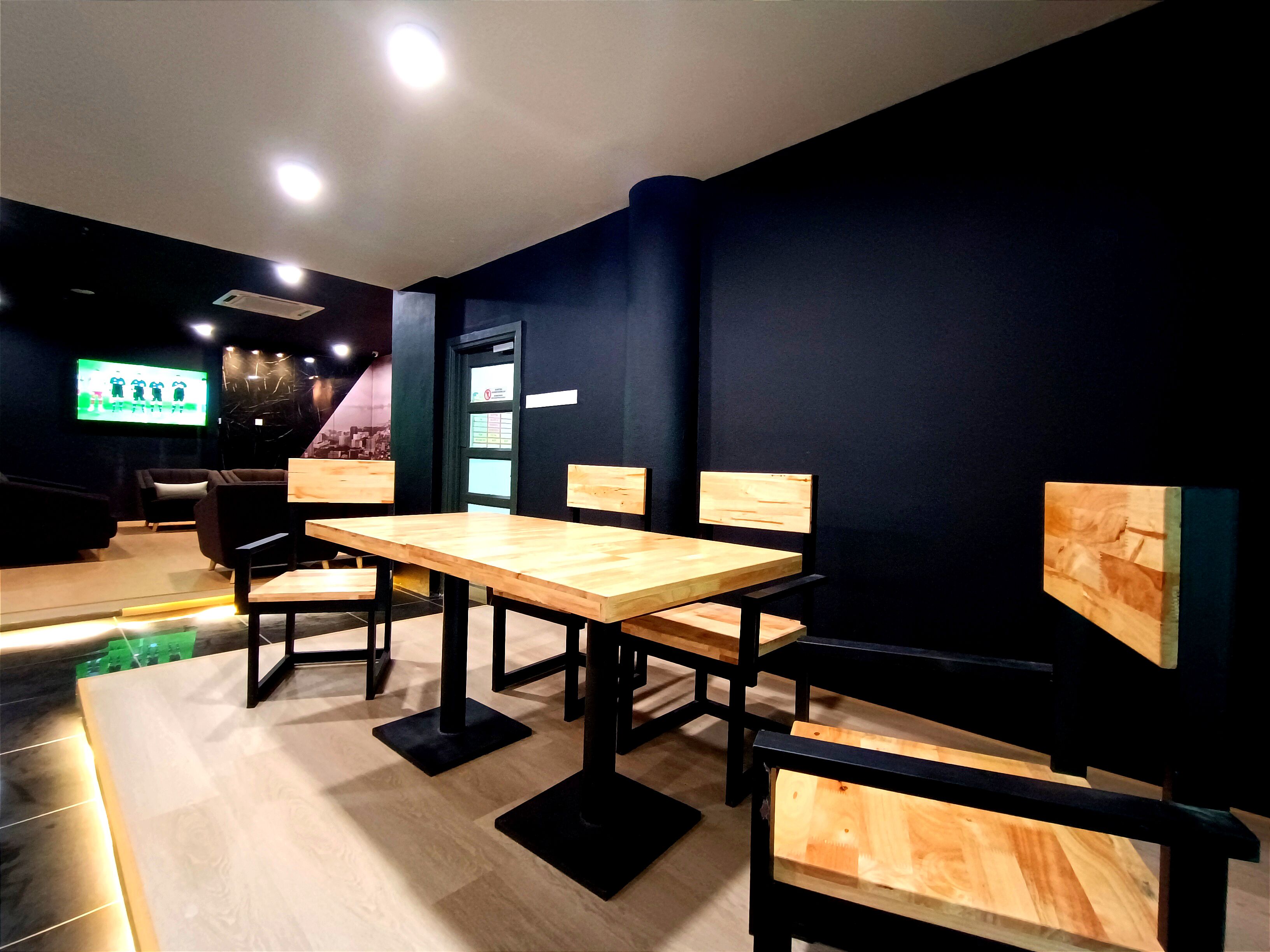 A modern interior with wooden tables and chairs, a dark wall, and a screen displaying a game.