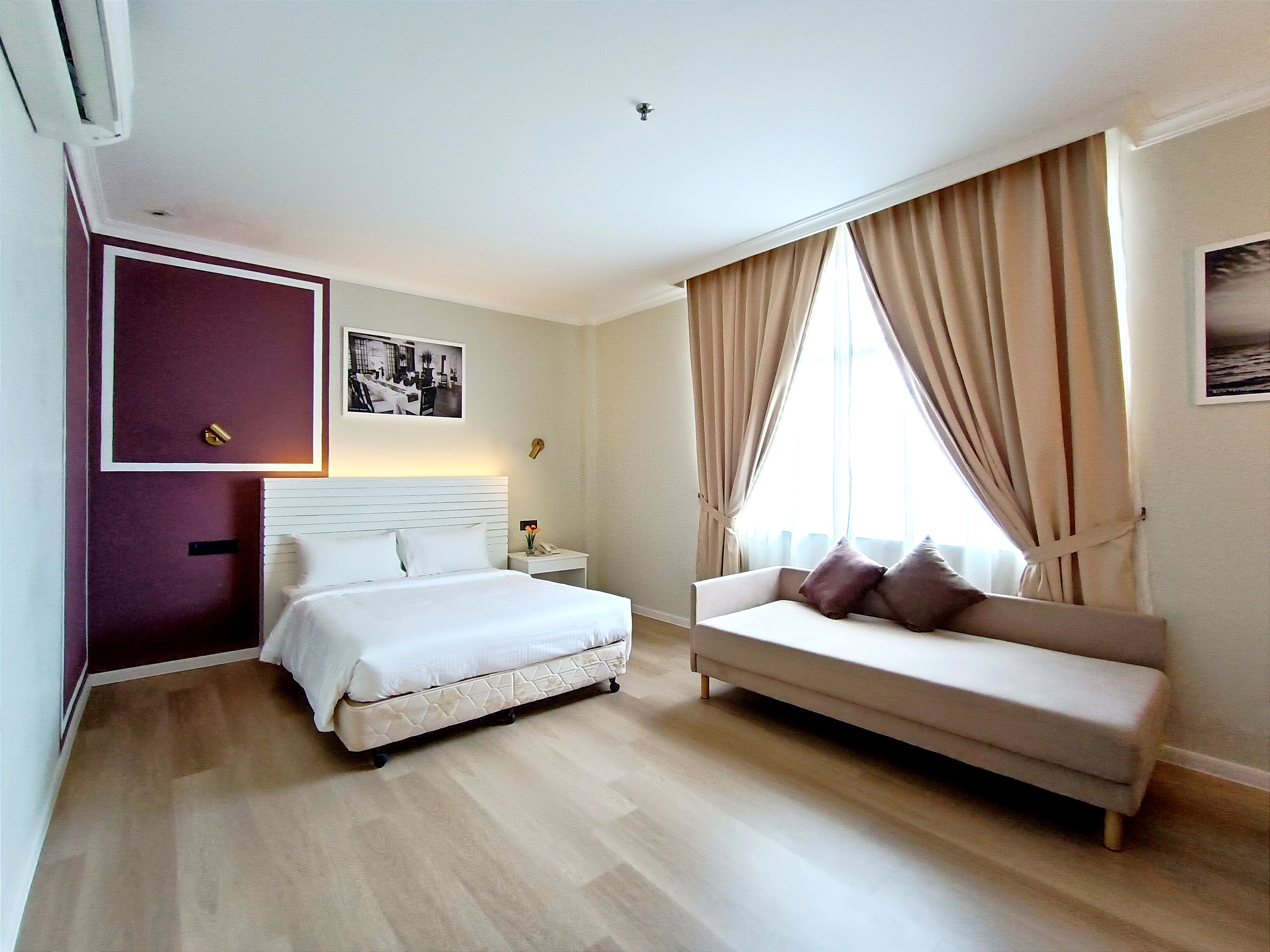 Een hotelkamer met een bed, een bank, een nachtkastje en een raam met gordijnen.