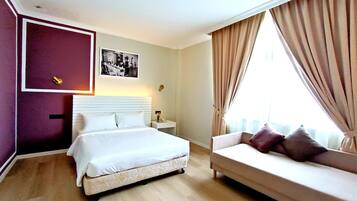 A hotel room with a bed, a sofa, a nightstand, a lamp, a picture on the wall, and curtains on the window.
