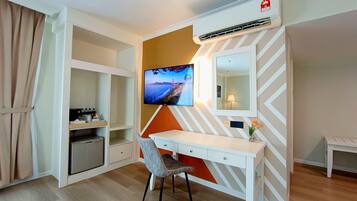 Habitación de hotel con escritorio, silla, televisión, aire acondicionado y un estante pequeño con artículos de aseo.
