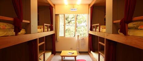 Un dormitorio con literas, una mesita pequeña y una ventana con vistas a árboles.