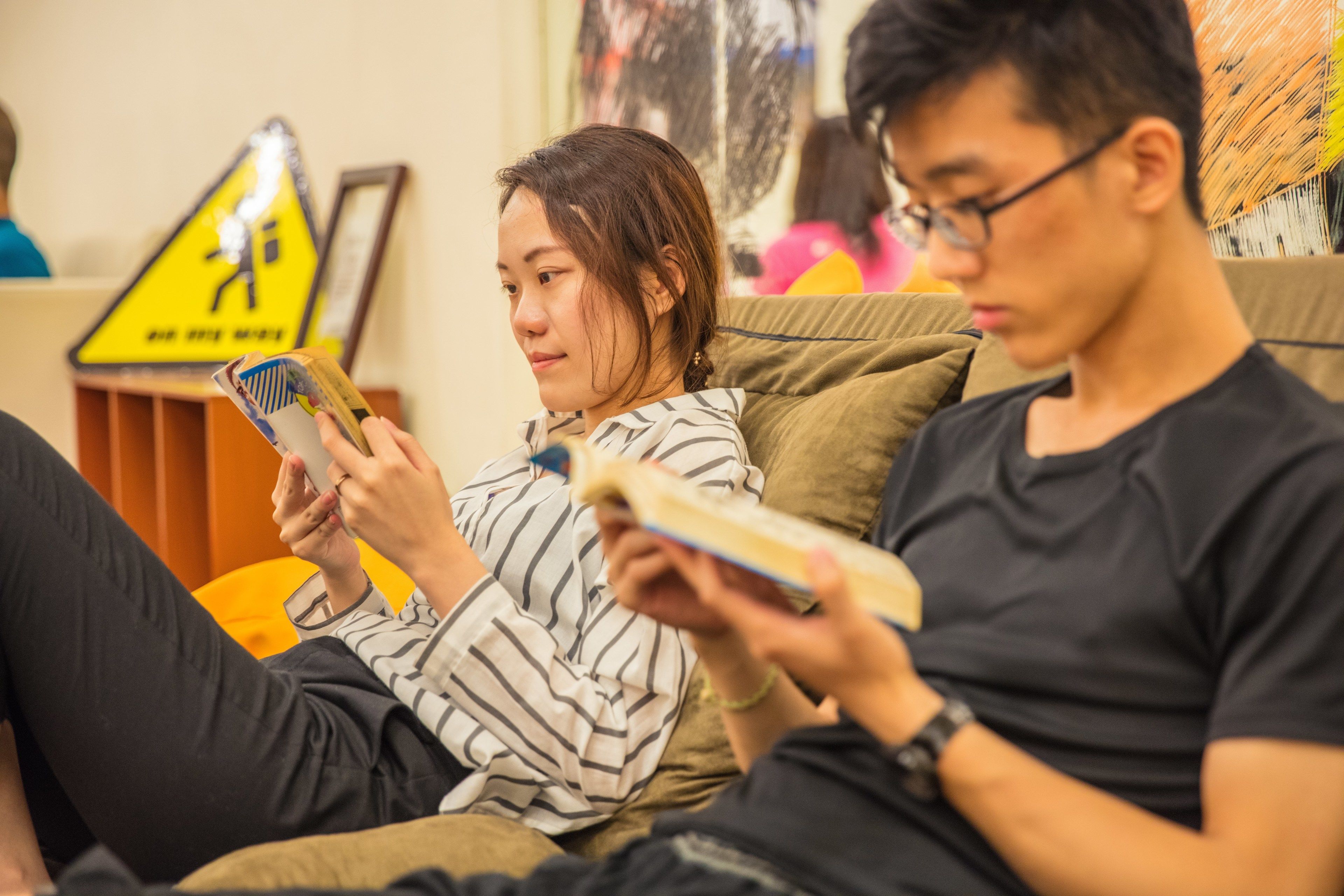 Une pièce avec un canapé, une personne qui lit un livre et une autre personne qui utilise un téléphone intelligent.