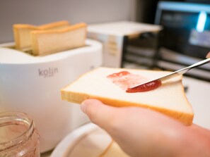 A slice of white bread with red jam being spread by a knife. - On My Way Taipei Youth Hostel (Taipei)
