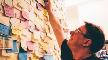 Una persona interactuando con una pared llena de notas y documentos.