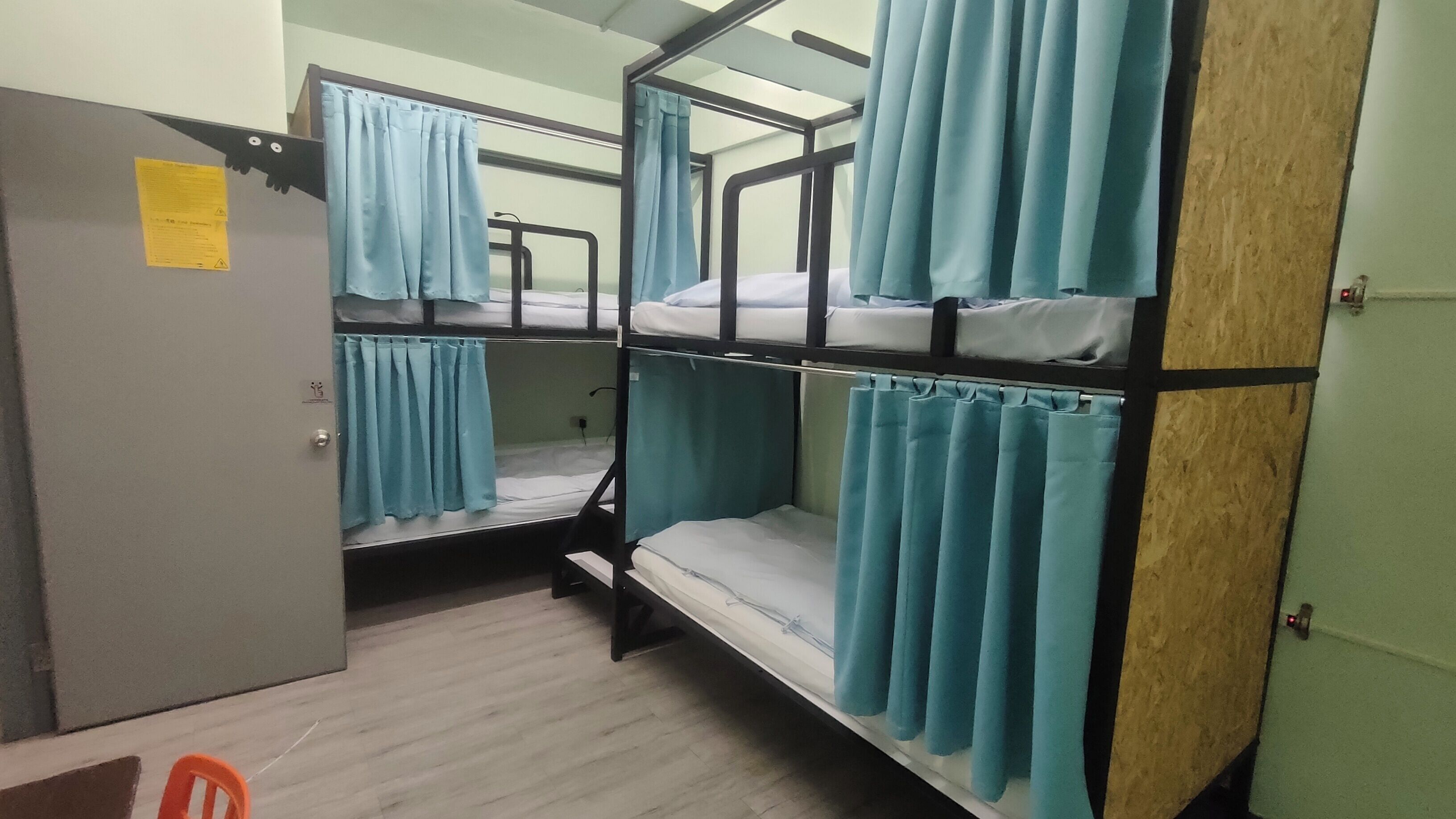 A bunk bed room with blue curtains, a wooden door, and a small orange chair.