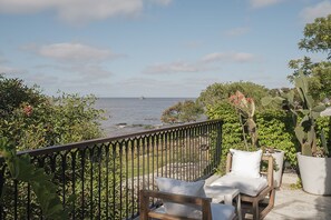 A balcony with a view of the ocean, a wooden chair with a cushion, and potted plants. - Charco Hotel (Colonia del Sacramento)