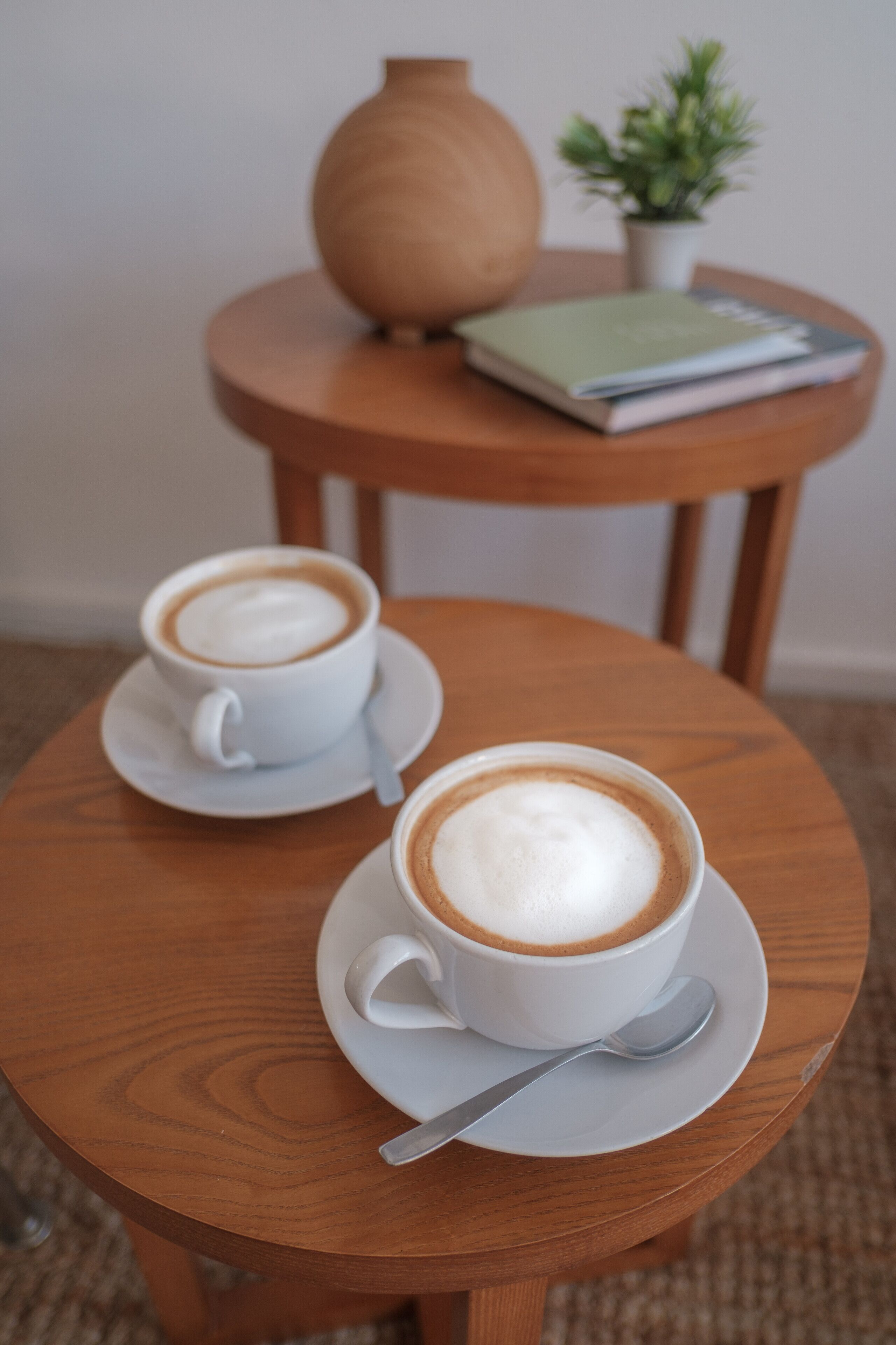 Dos tazas de café sobre una mesa redonda de madera, con cuchara y platillo.