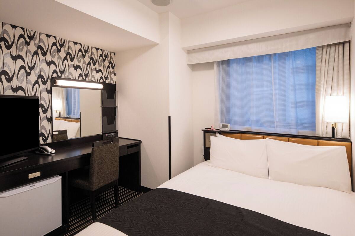 Habitació d'hotel amb un llit, escriptori, televisió, mirall i finestra amb cortines.