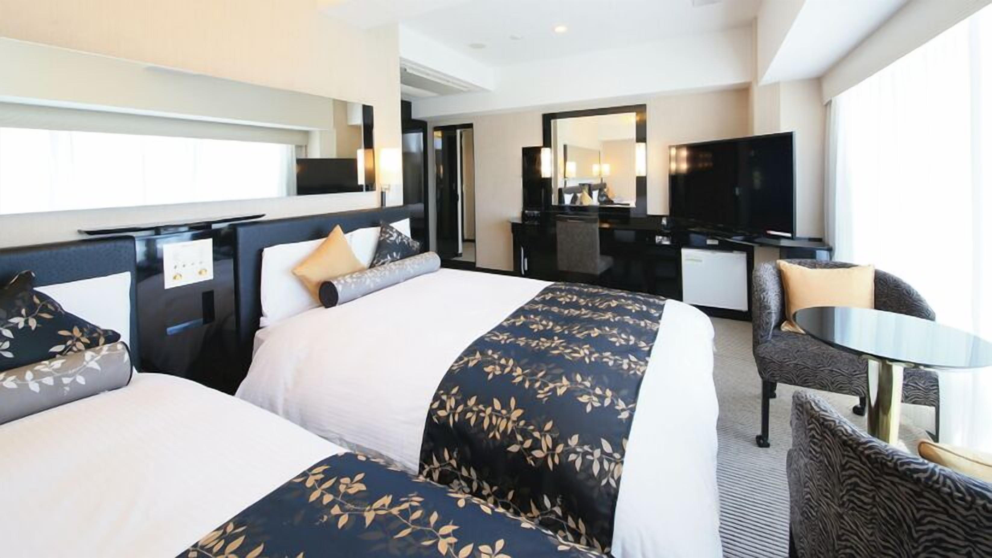 A hotel room with two beds, a desk, a chair, a TV, and a large window.