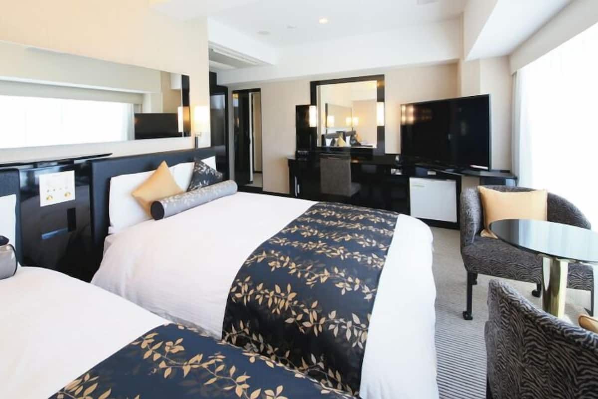 Une chambre d’hôtel avec deux lits, un bureau, une chaise, une télévision et une grande fenêtre.