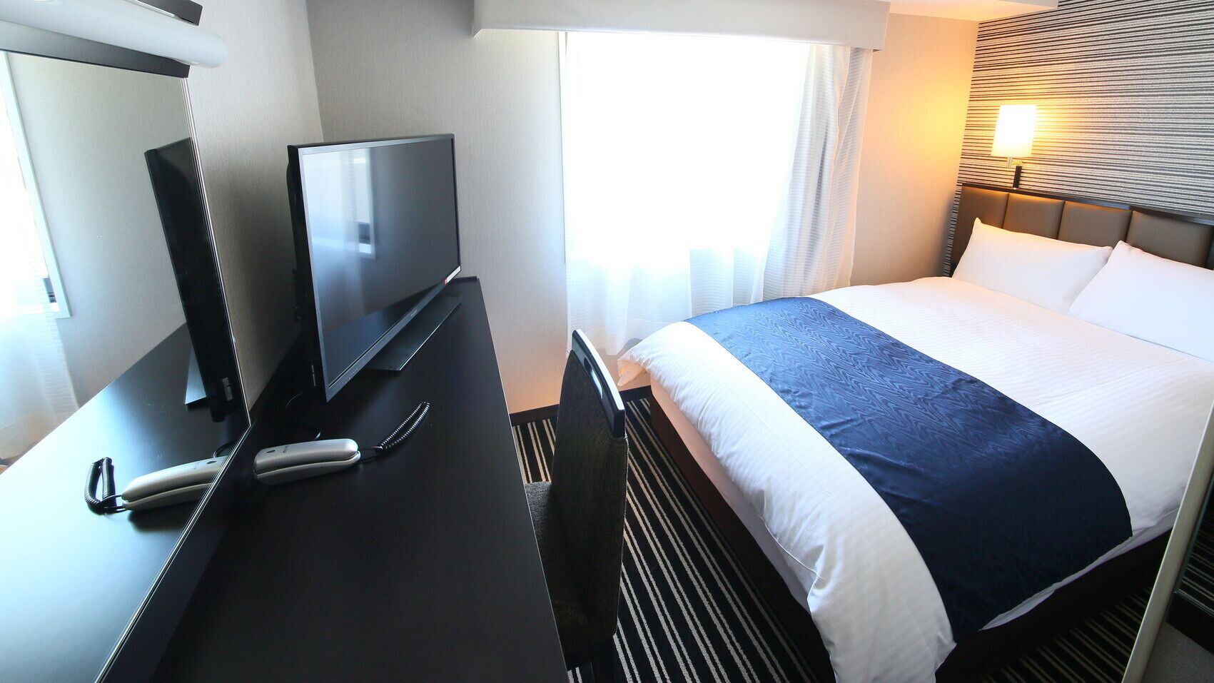 A hotel room with a bed, a TV, a desk, and a lamp.