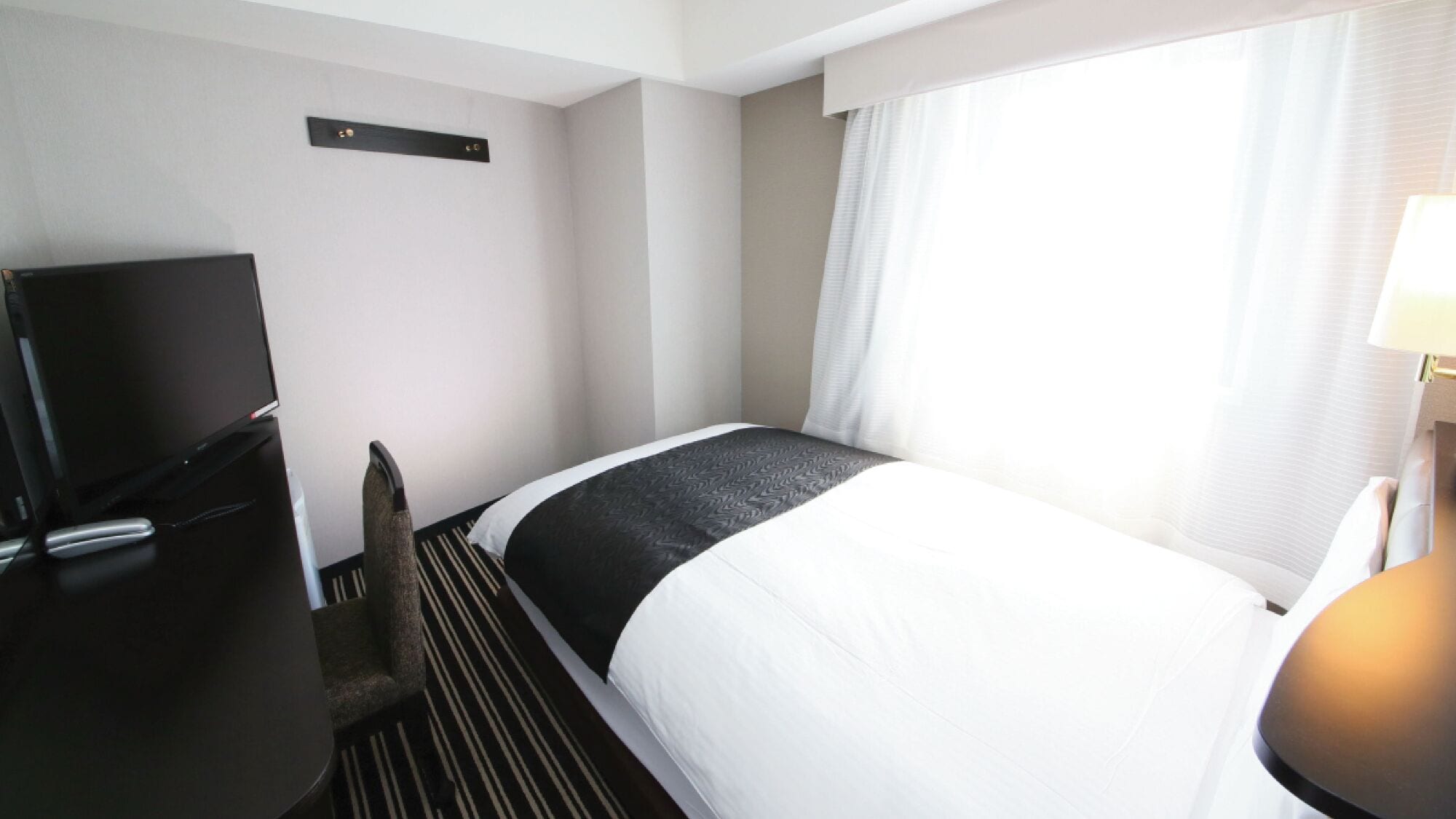 Una camera d'albergo con un letto, una televisione, una scrivania e una lampada.