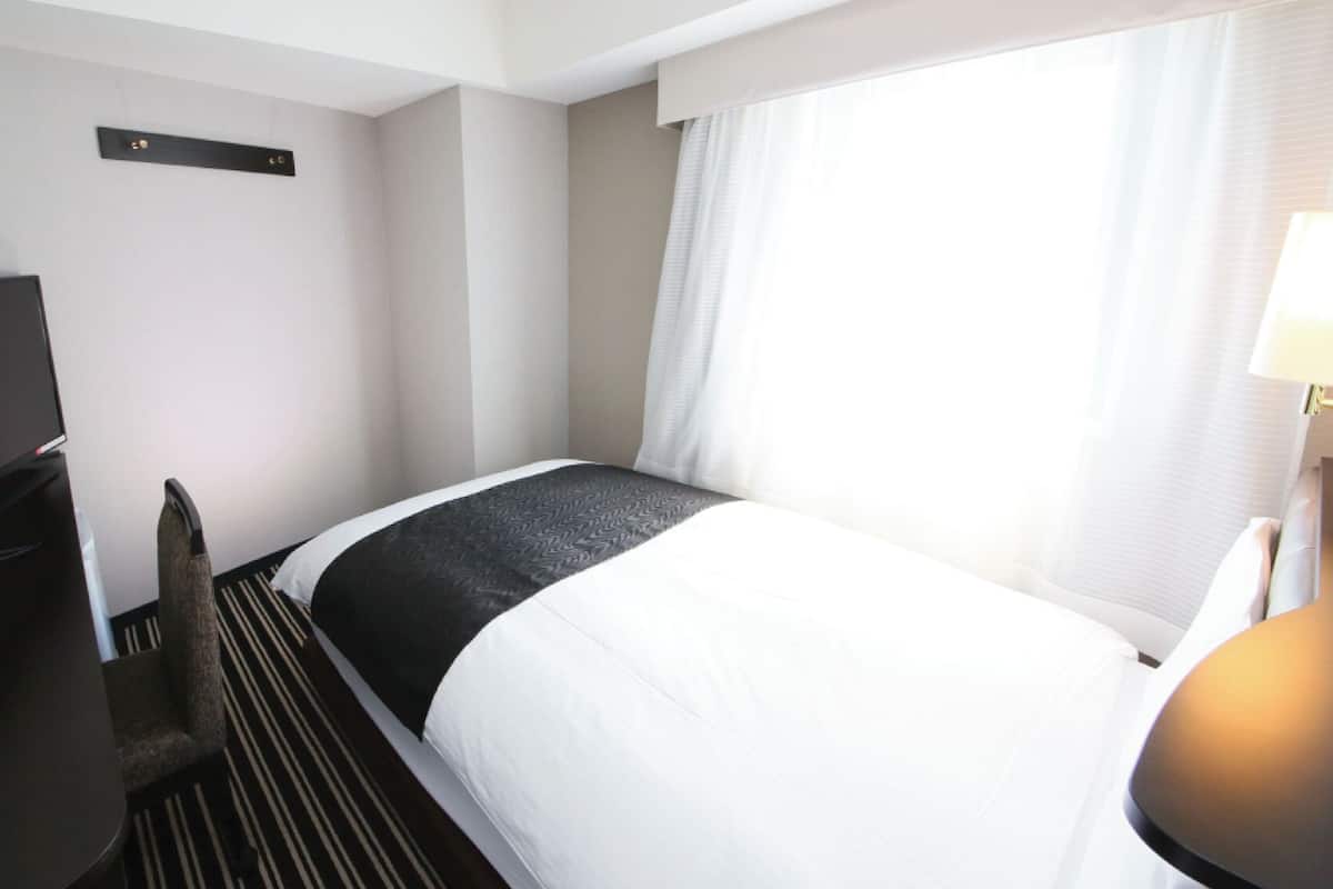 A hotel room with a bed, a television, a desk, and a lamp.