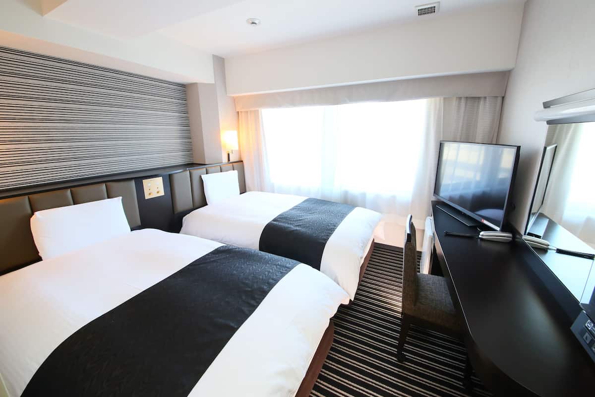 A hotel room with two beds, a flat-screen TV, and a desk with a computer.
