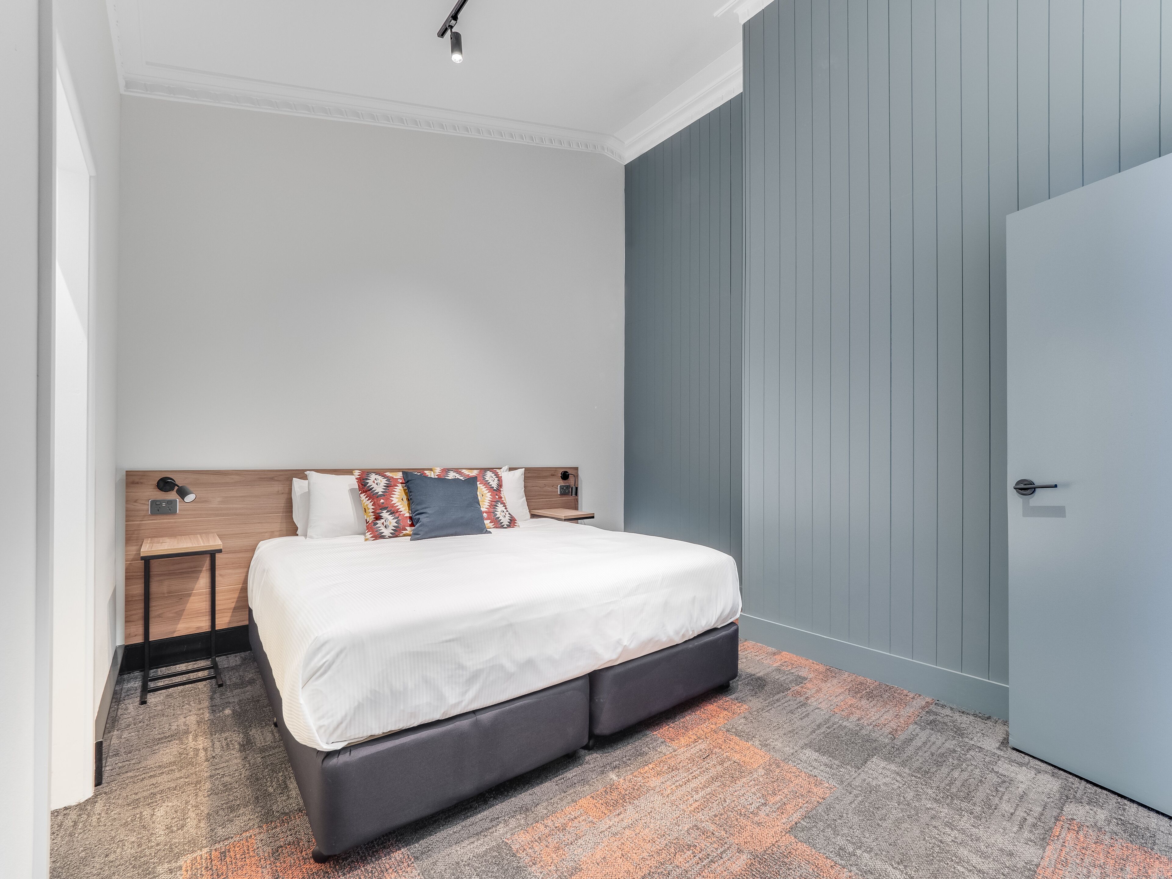 Ein modernes Hotelzimmer mit einem großen Bett, einem Nachttisch, einer Wandlampe und einer Tür.