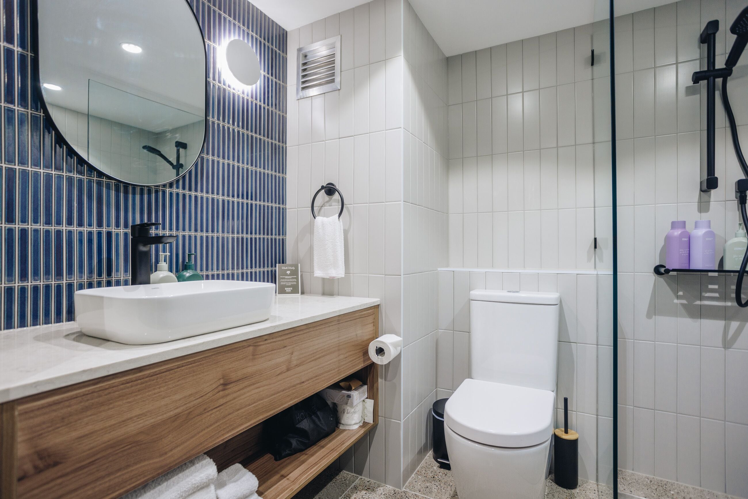 A modern bathroom with a white sink, wooden vanity, a toilet, and a glass shower enclosure.
