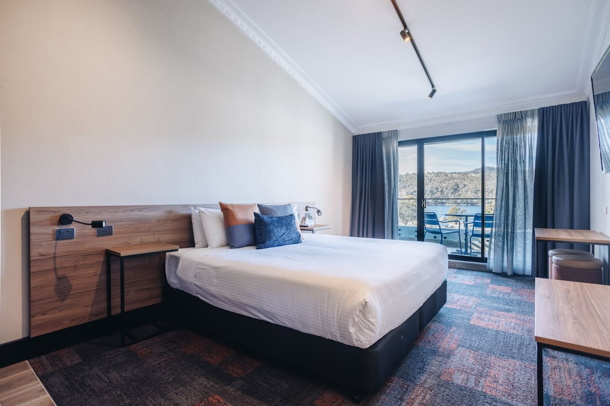Habitación de hotel con una cama grande, cabecero de madera, escritorio y vistas al exterior.