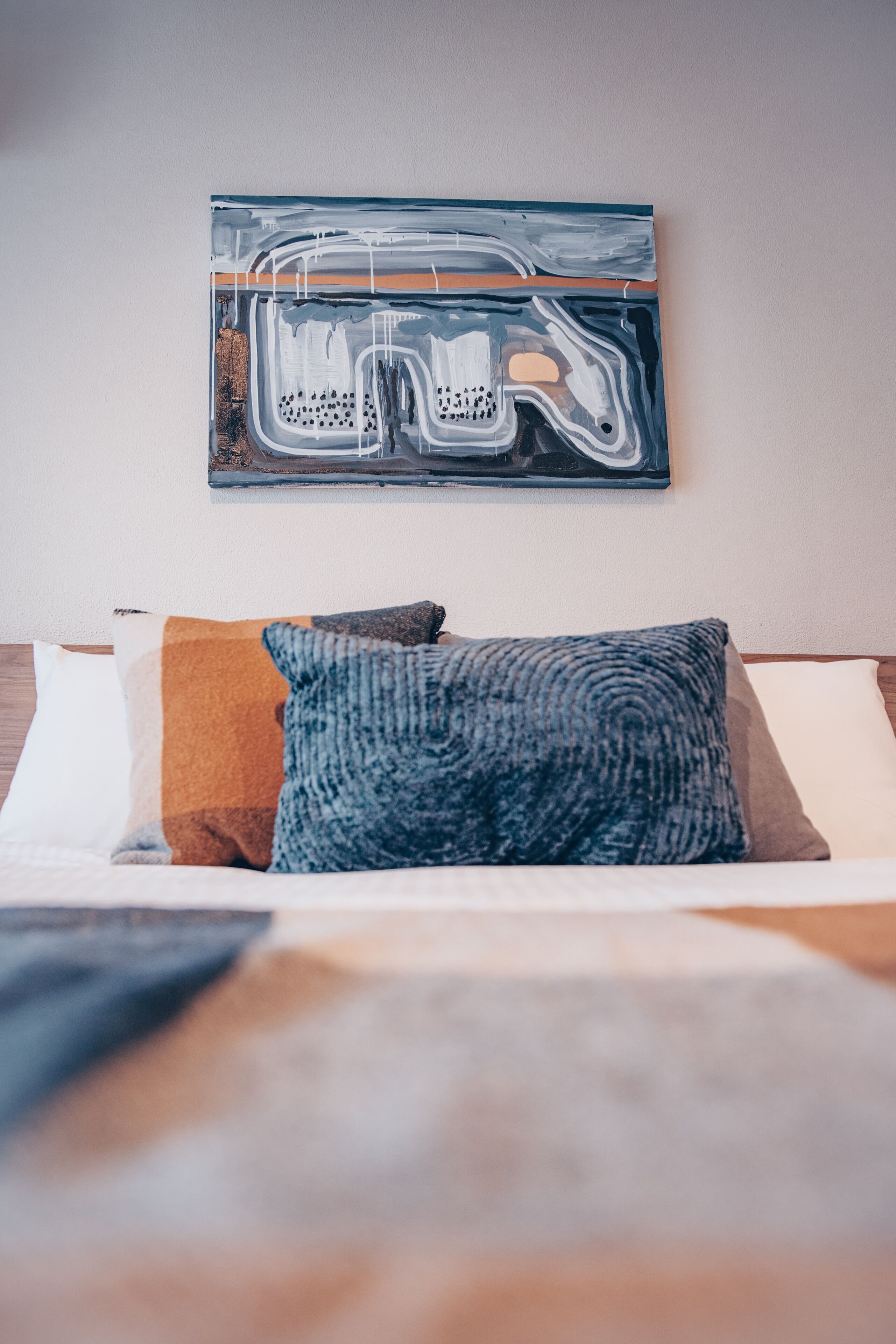 Uma cama com um cobertor colorido e um travesseiro, um quadro abstrato na parede e uma cabeceira de madeira.