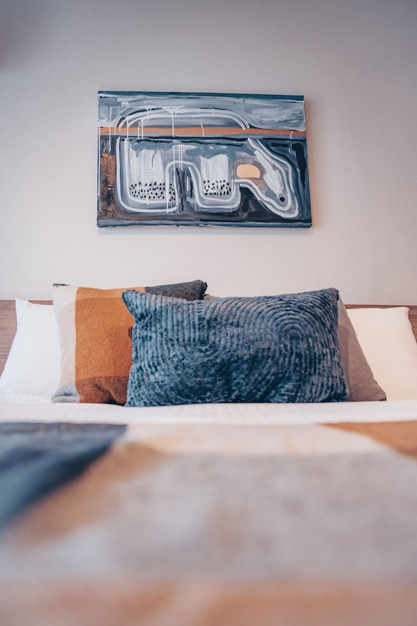 Una cama con un edredón colorido y una almohada, un cuadro abstracto colgado en la pared y un cabecero de madera.