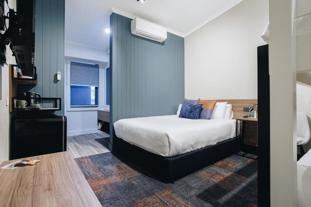A modern hotel room with a large bed, a desk, and a small kitchenette.