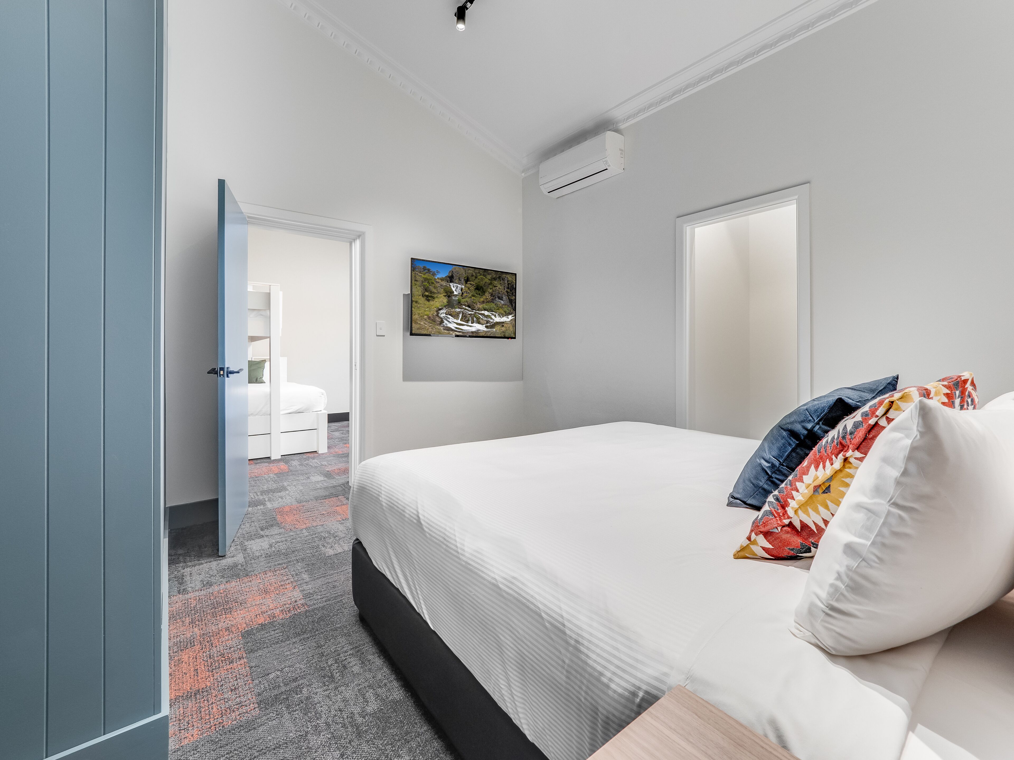 A modern hotel room with a large bed, a flat-screen TV mounted on the wall, and a door leading to a bathroom.
