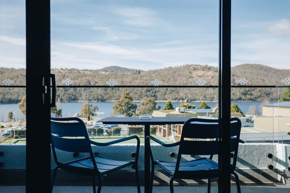 Un balcón con dos sillas y una mesa, con vista a un lago y colinas.