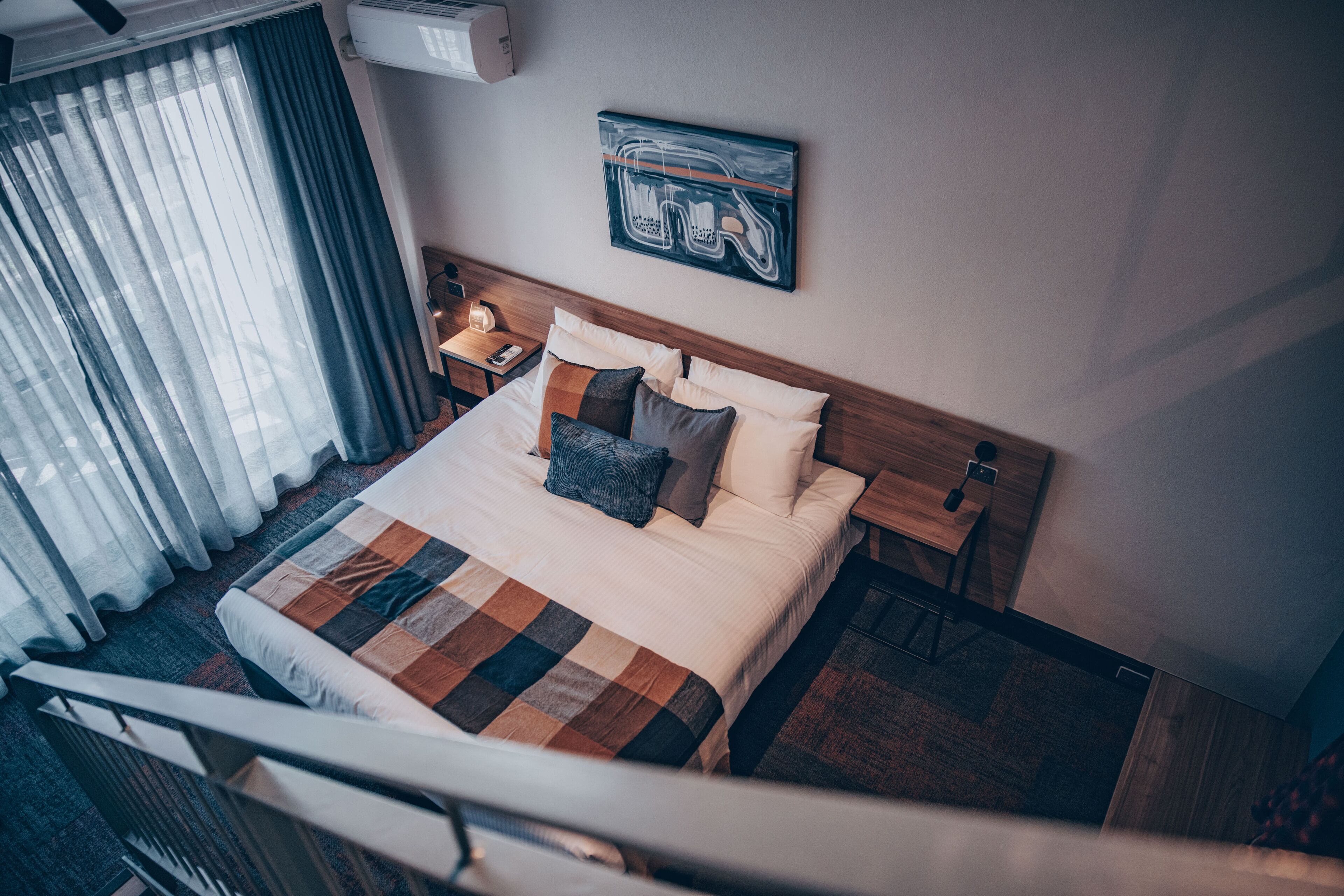 Una habitación de hotel con una cama grande, una mesita de noche, una lámpara y una obra de arte colgada en la pared.