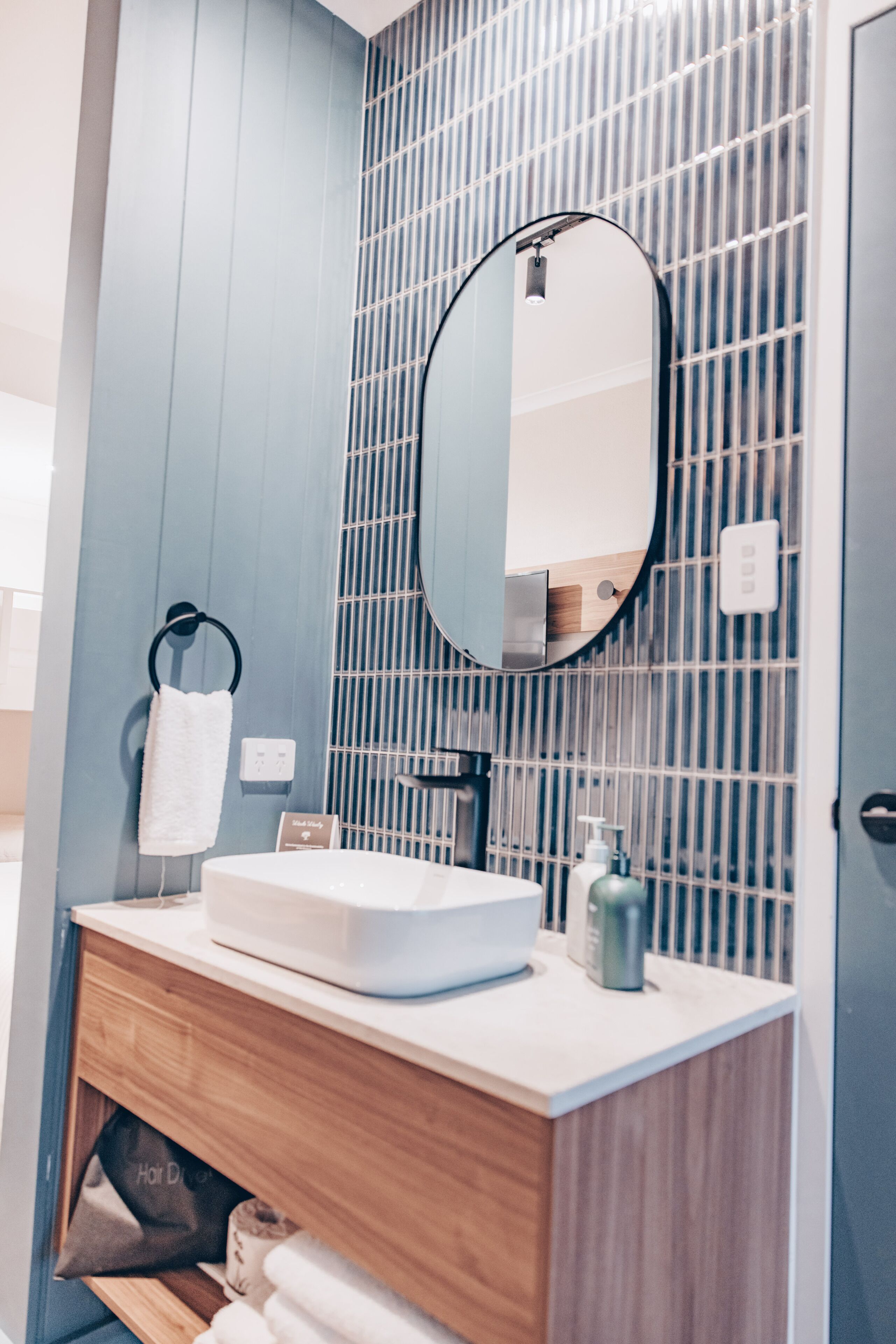 Een moderne badkamer met een houten wastafelmeubel, een witte wasbak, een spiegel en een handdoekrek.