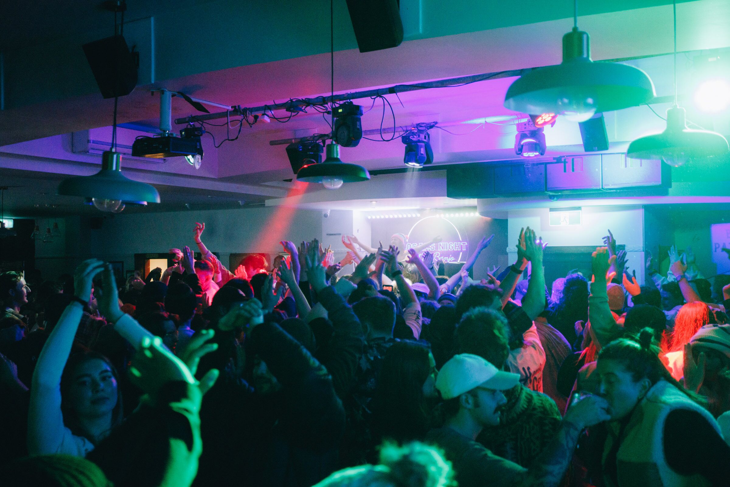 A crowded indoor space with people raising their hands, possibly at a concert or event.