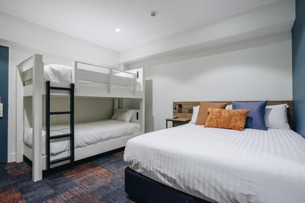 Een hotelkamer met een stapelbed, een eenpersoonsbed en een nachtkastje.