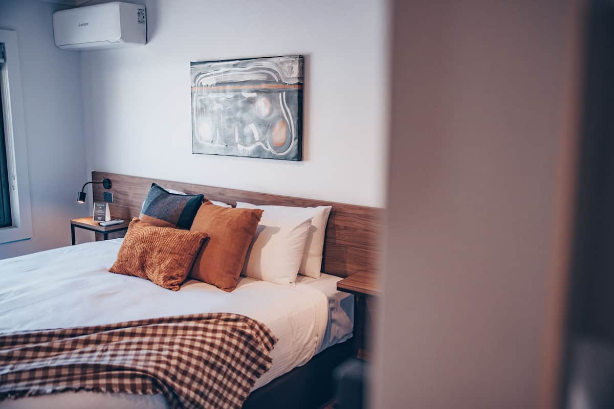 Una cama bien hecha con una colcha a cuadros, un cabecero de madera y un cuadro abstracto colgado en la pared.