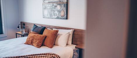 Una cama bien hecha con una colcha a cuadros, un cabecero de madera y un cuadro abstracto colgado en la pared.