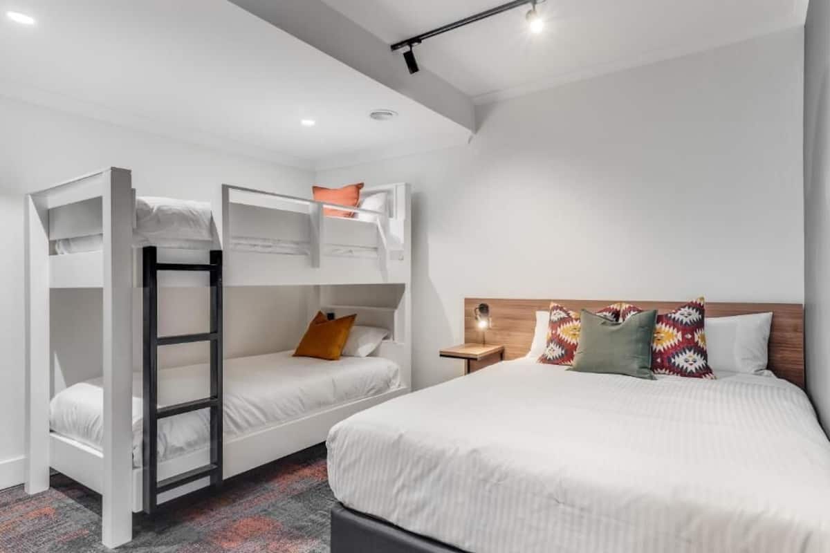Una habitación de hotel con literas, una cama grande y una mesita de noche con lámpara.