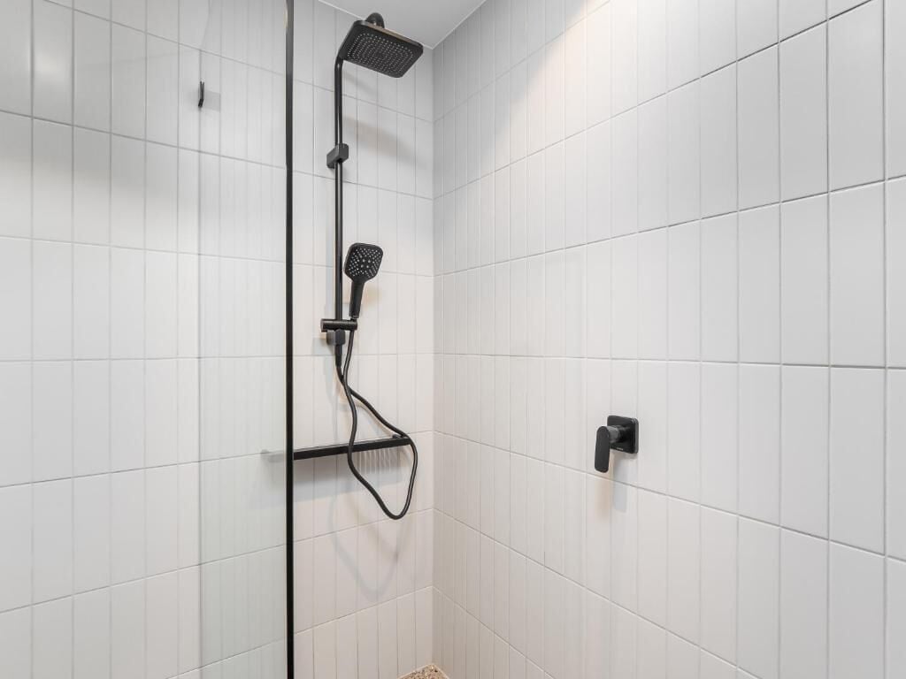 Ducha con cabezal de ducha de mano y panel de control en la pared.